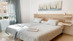 A double bed with a geometric patterned bedspread, a headboard with horizontal slats, and a painting of sailboats on the wall. - Center, 2 min.de the beach, with terrace, air conditioning and heating. (Nerja)