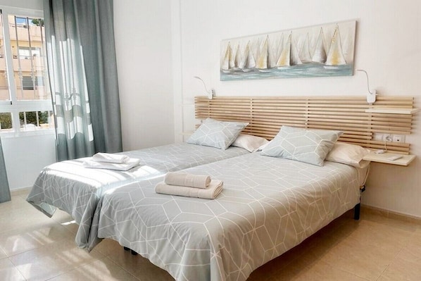 A double bed with a geometric patterned bedspread, a headboard with horizontal slats, and a painting of sailboats on the wall. - Downtown, 2 minutes from the beach, with a terrace, air conditioning, and heating. (Nerja)