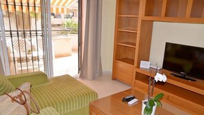 A room with a green sofa, a wooden TV stand, a small table with a remote and a potted plant. - Center, 2 min.de the beach, with terrace, air conditioning and heating. (Nerja)