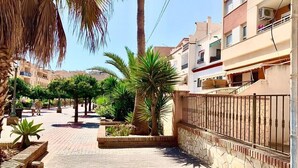 A paved walkway lined with palm trees and planters, leading to a building with a stone wall and metal railing. - Center, 2 min.de the beach, with terrace, air conditioning and heating. (Nerja)