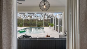 A poolside area with a covered patio, outdoor seating, and a hanging light fixture. - Tropical Retreat - Oversized heated pool, golf, pickle-ball, tennis, bikes, (Rotonda West)