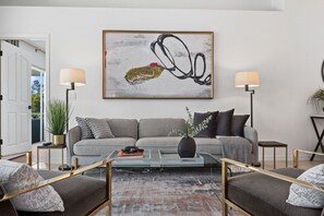 A modern living room with a grey sofa, two side tables, a coffee table, and a large abstract painting on the wall.