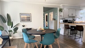 Una cocina moderna con armarios blancos, un comedor con sillas color turquesa y una planta grande.