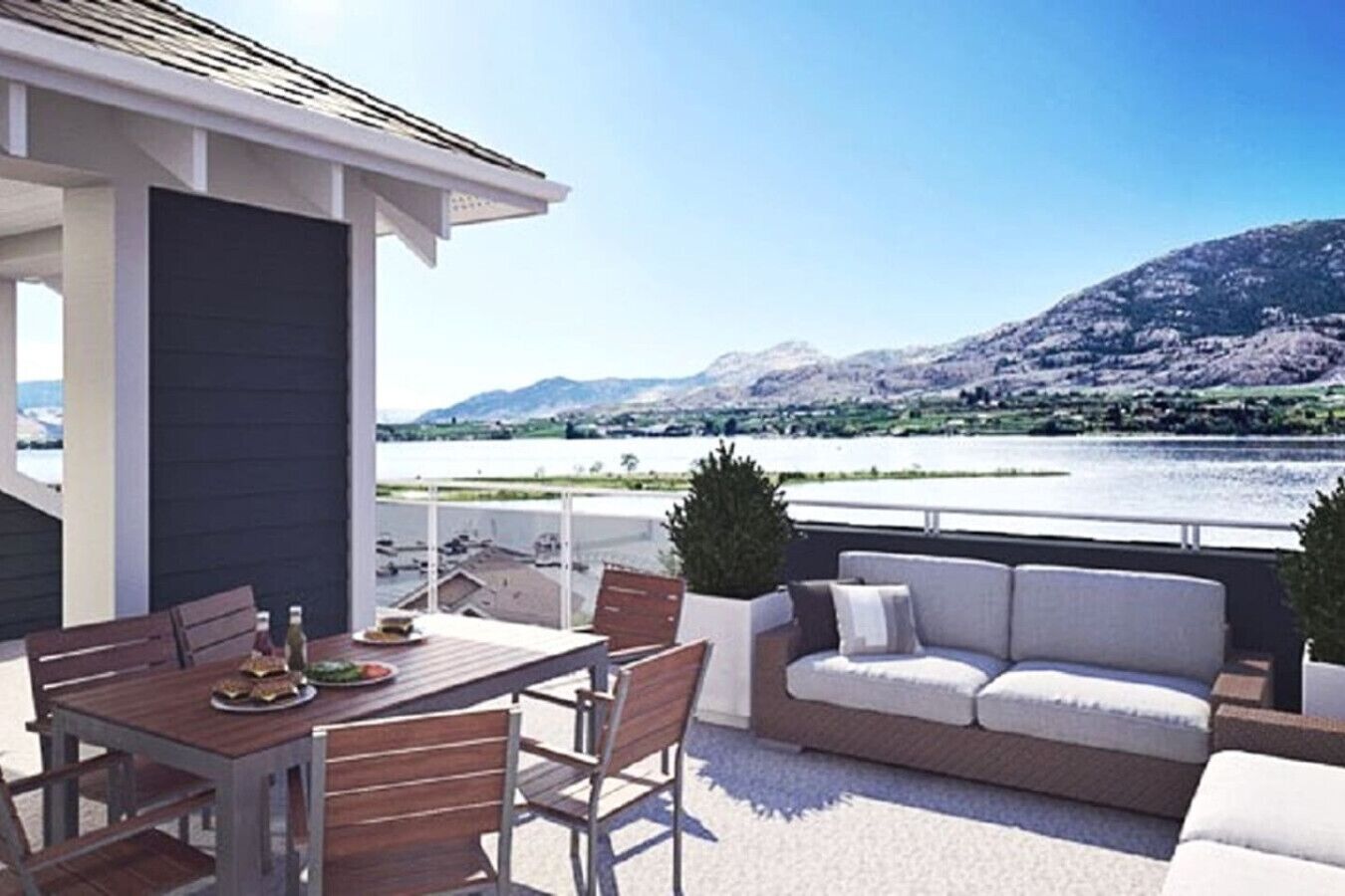 En terrasse med bord og stole, en sofa, samt udsigt til en sø og bjerge.