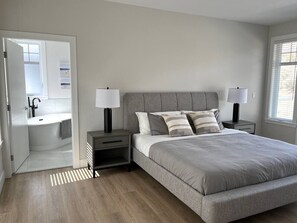 A bedroom with a large bed, bedside tables, a nightstand, a lamp, a mirror, and a bathroom with a bathtub.