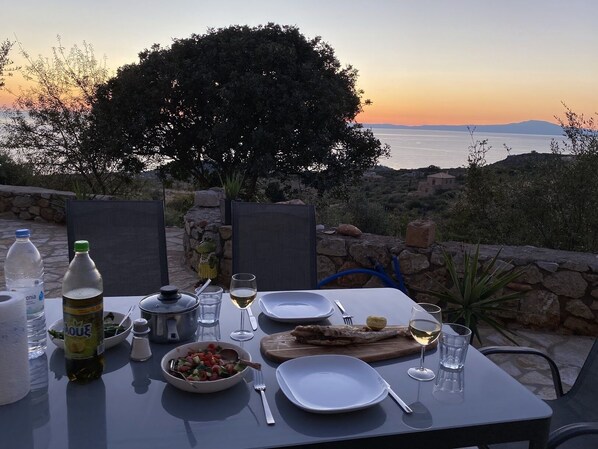 An outdoor dining table set with plates, cutlery, a bowl of salad, a bottle of olive oil, a glass of wine, and a water bottle.