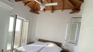 Una camera da letto con soffitto in legno, un letto con copriletto bianco, una ventola a soffitto e un'ampia finestra.