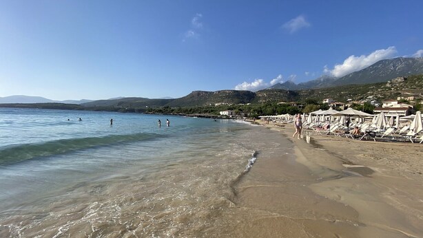 Una spiaggia con acque cristalline, lettini e ombrelloni.