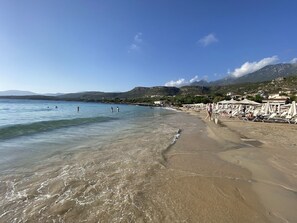 A beach with clear water, a sandy shore, and a backdrop of hills.