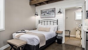 Une chambre à coucher comprenant un lit, des tables de chevet, un banc, une poubelle et un panneau fixé au mur.