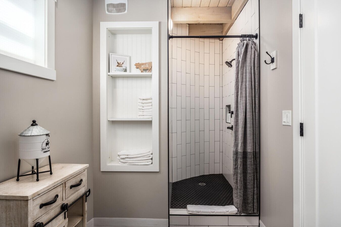 A bathroom with a shower, a towel rack, a shelf with towels and a sign, and a small table with a kettle.