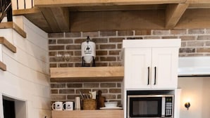 A kitchen with white cabinets, a brick backsplash, a microwave, and a sink.