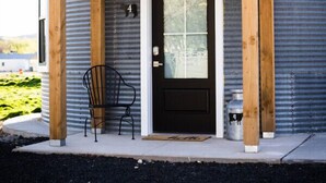 A building with a corrugated metal exterior, a wooden porch with a black door, and a black chair.
