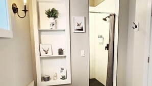 A modern bathroom with a freestanding bathtub, a wall-mounted shelf with decorative items, and a door leading to another room.