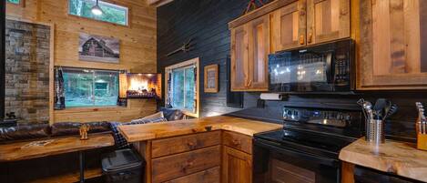 A rustic kitchen with wooden cabinets, a black stove, and a microwave.