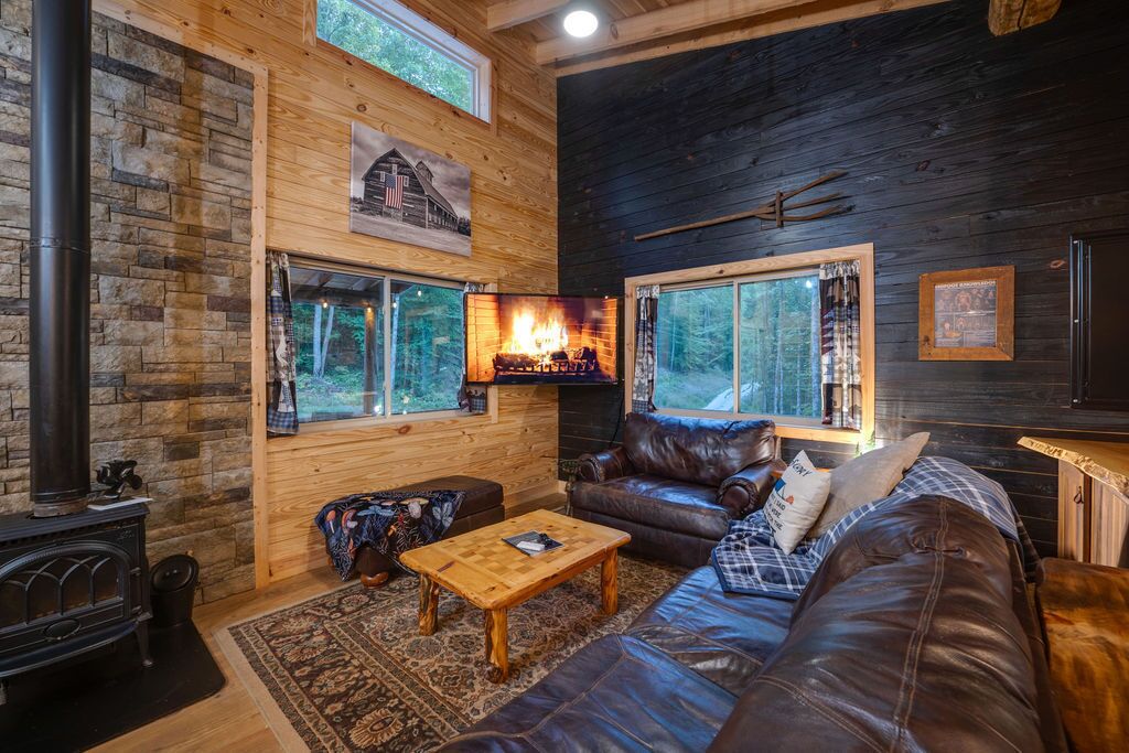 Un acogedor interior de cabaña con chimenea, sofá de cuero y suelo de madera rústica.