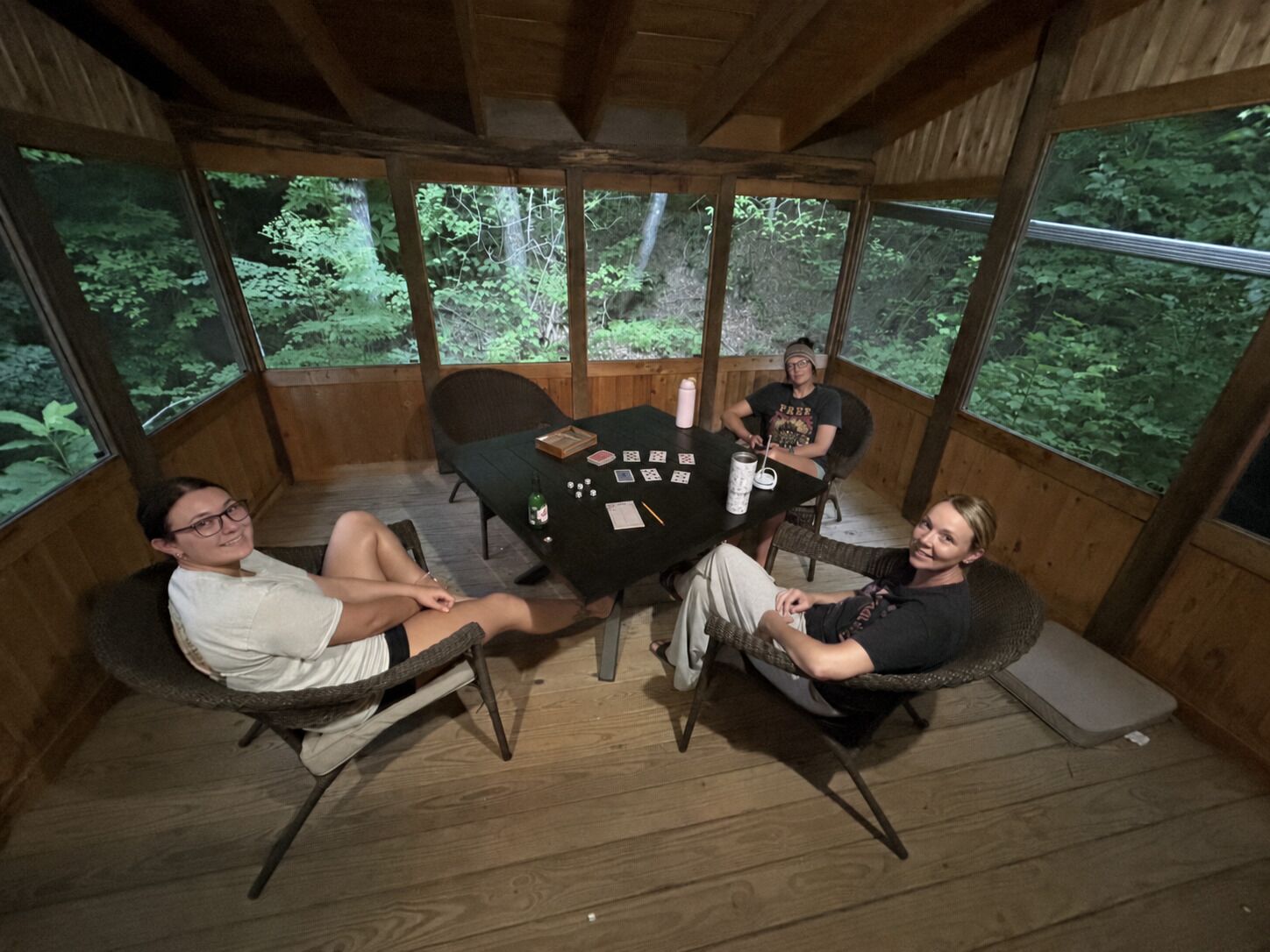 Una terraza de madera con una mesa y sillas, rodeada de grandes ventanales con vista al bosque.