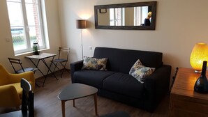 A living room with a sofa, a small table, a chair, a lamp, and a window with a view of the outside. - Elegant Studio, facing marina and harbour (Fécamp)