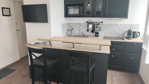 A compact kitchen with a wooden island, black bar stools, a microwave, and a coffee maker. - Elegant Studio, facing marina and harbour (Fécamp)