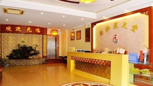 A hotel reception area with a reception desk, a decorative wall with Chinese characters, and a patterned floor design. - Peigen Yizutang Hotel (Huizhou)