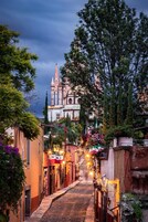 Una estrecha calle adoquinada bordeada por edificios con balcones, que conduce a una iglesia hist órica con una alta aguja.