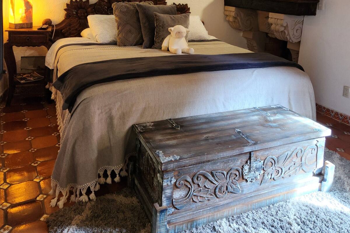 A cozy bedroom with a bed, a nightstand, a decorative lamp, and a wooden chest.