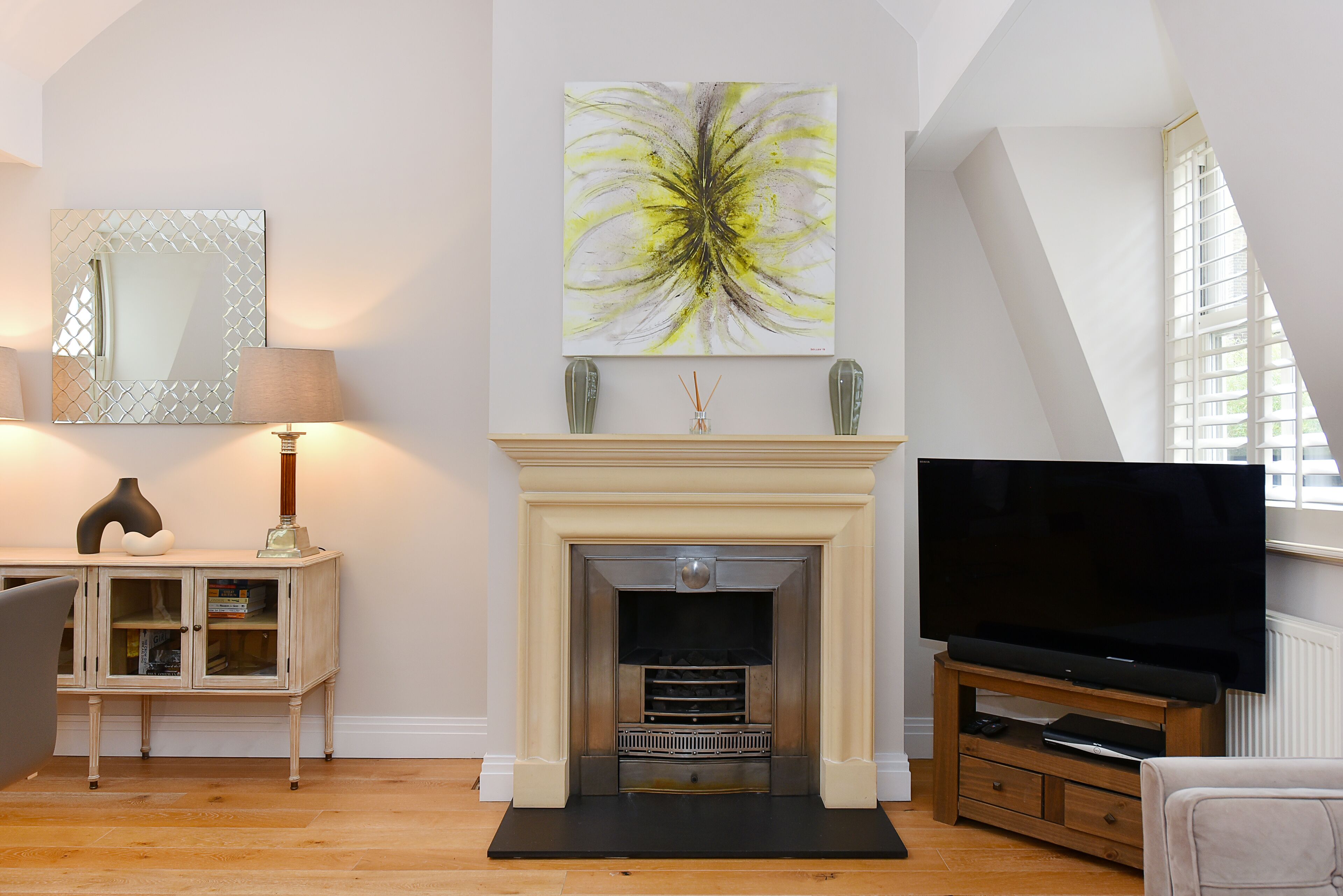 A living room with a fireplace, a television, and a large abstract painting.
