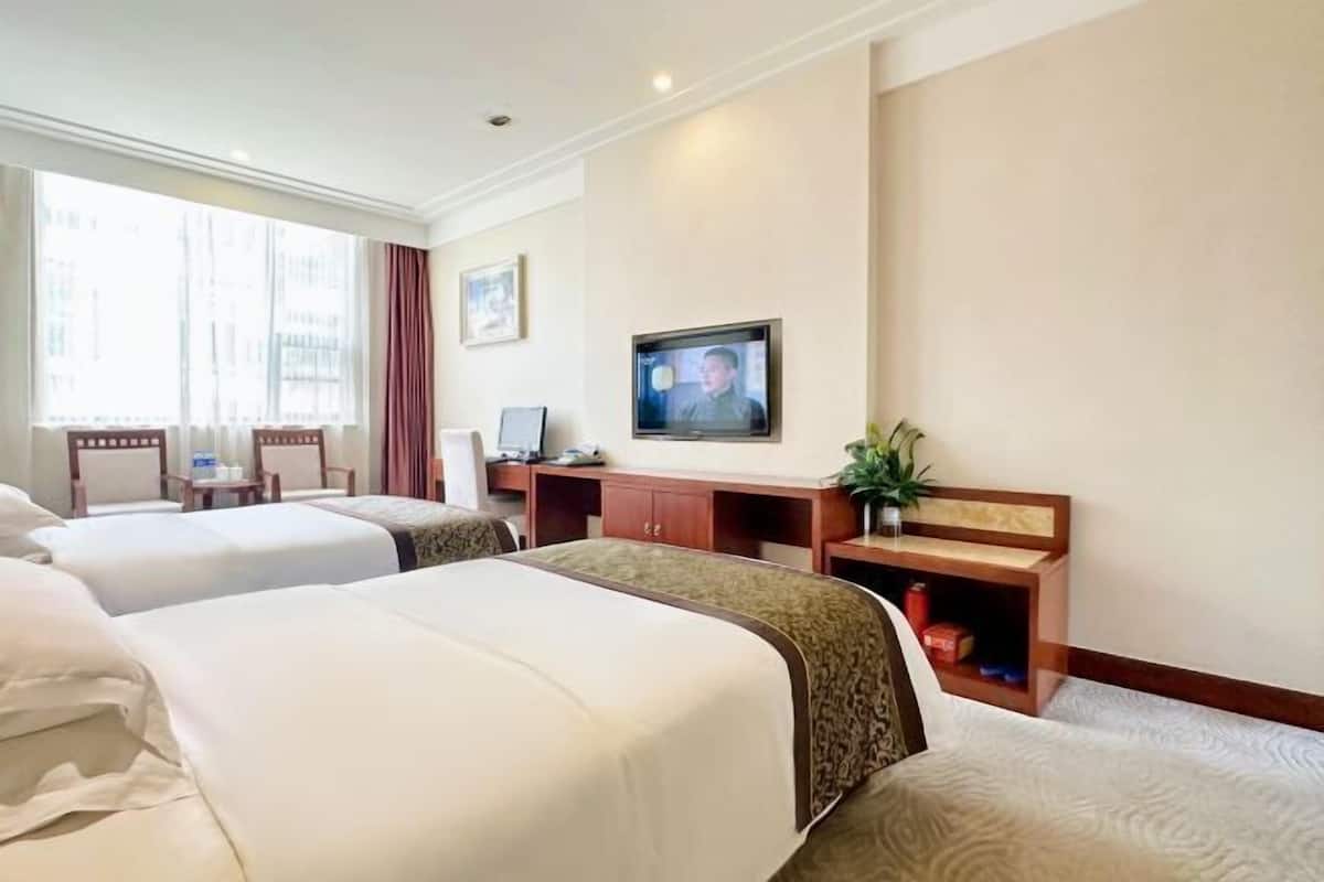 A hotel room with three beds, a desk with a computer, a TV, and a window with curtains.