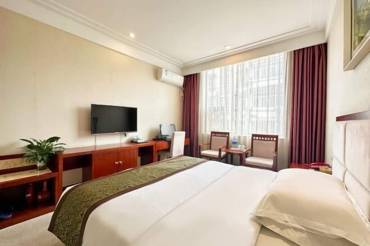 A hotel room with a large bed, a desk with a computer, a TV, and a seating area with chairs.