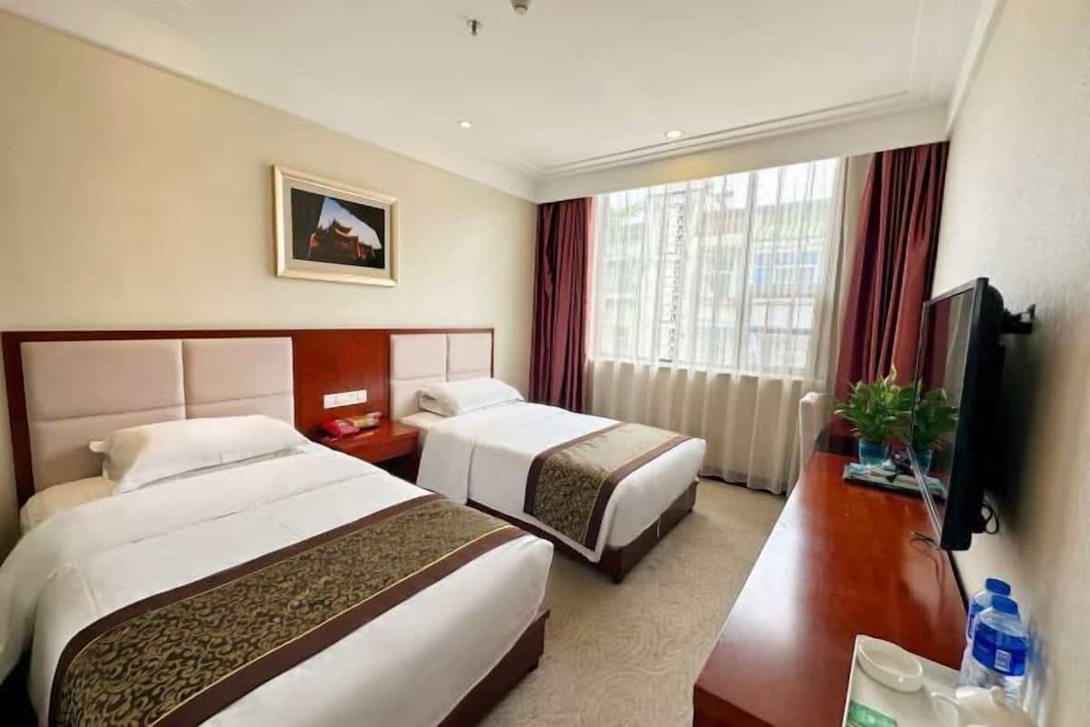 A hotel room with two beds, a wooden desk, a television, and a window with curtains.