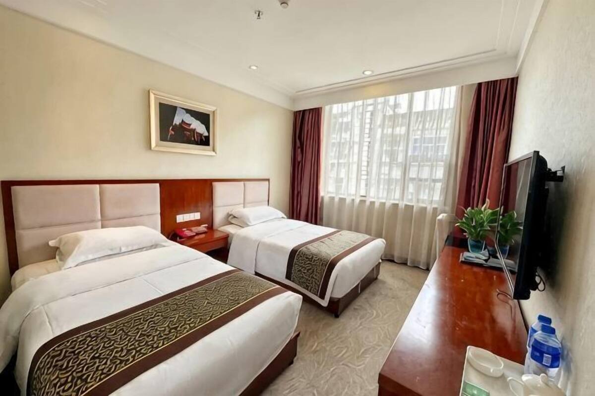 A hotel room with two beds, a desk, a television, and a window with curtains.