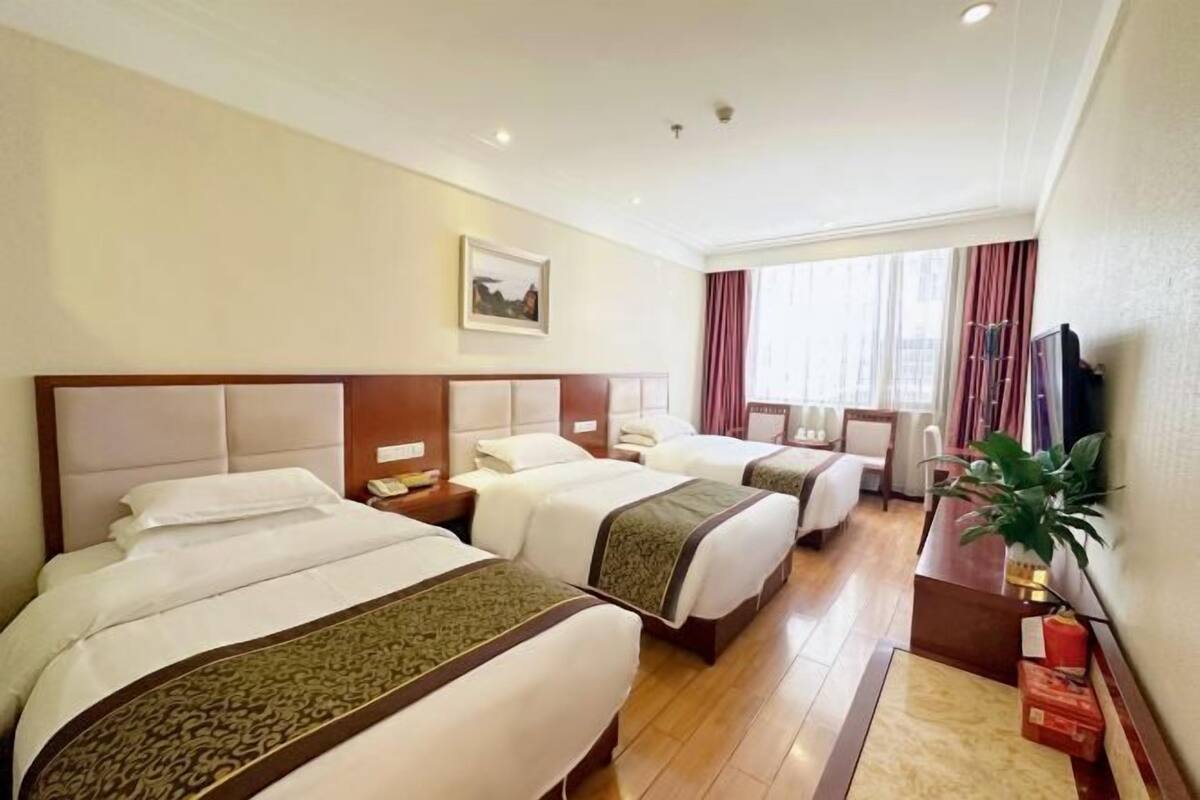 A hotel room with three beds, a television, a desk, and a window with curtains.