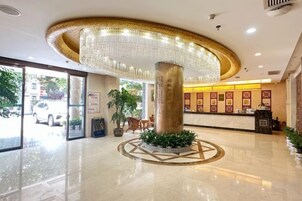 Un vestíbulo de hotel con una columna central, un mostrador de recepción y una gran araña.