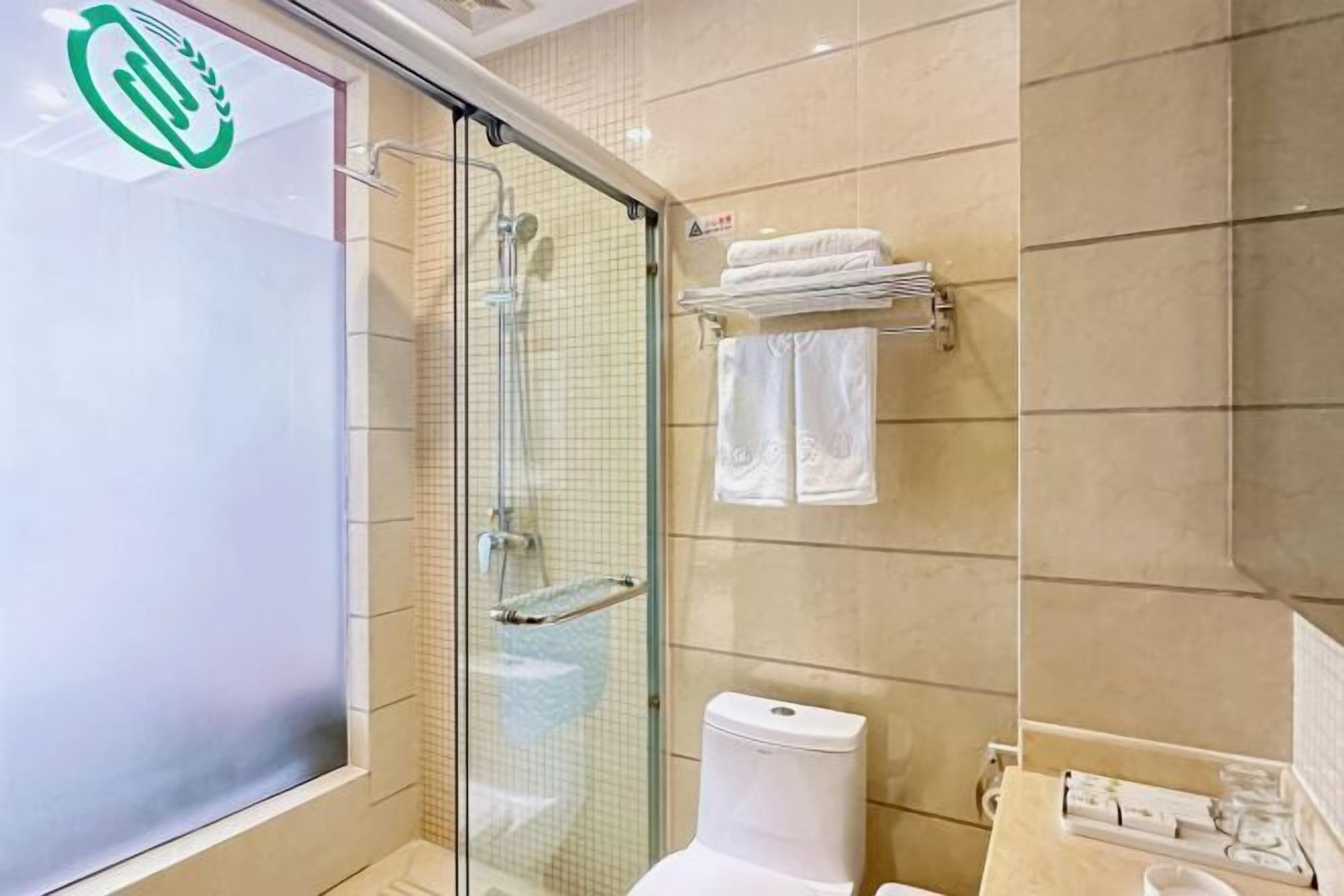 A bathroom with a glass shower enclosure, a toilet, and a towel rack with folded towels.
