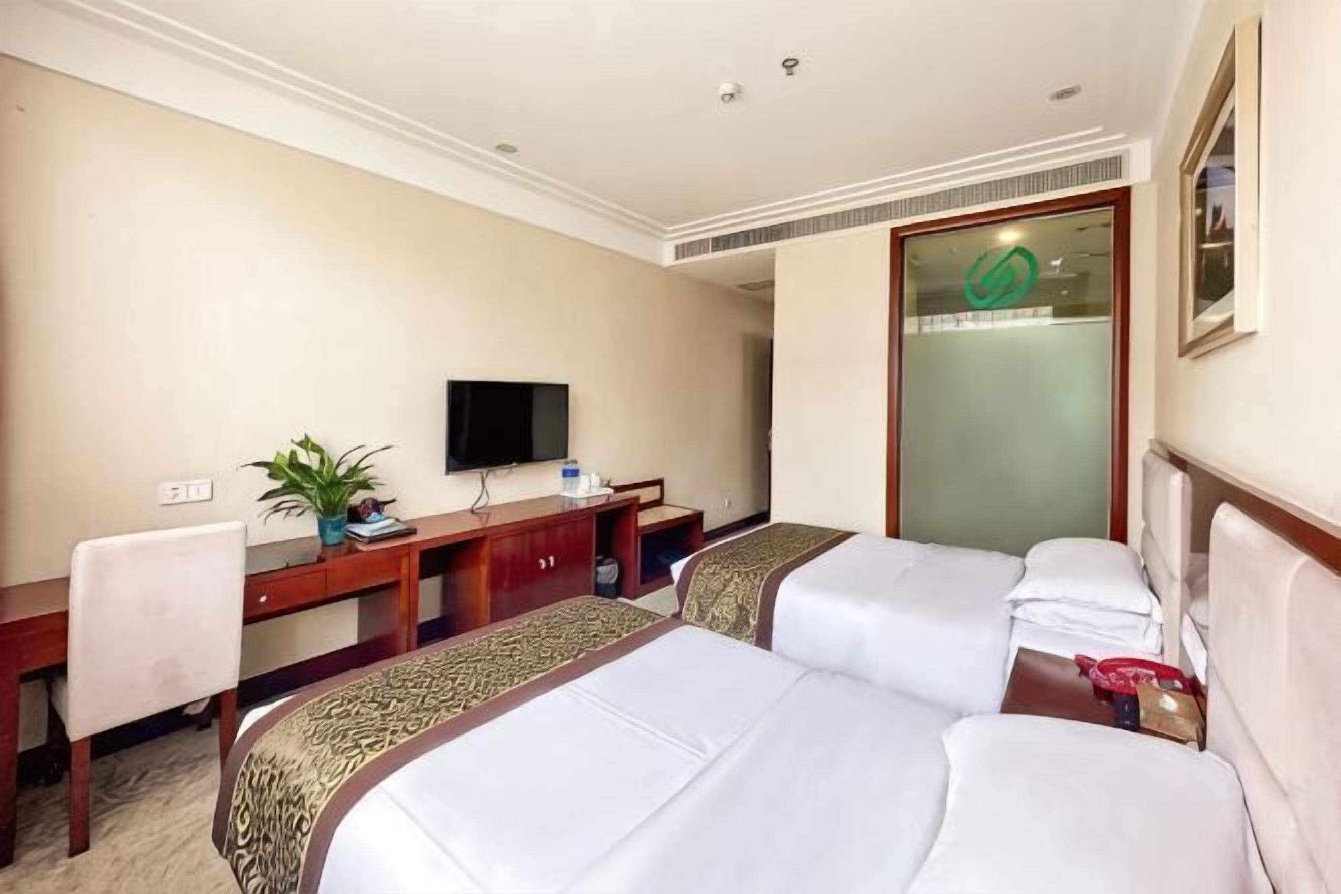 A hotel room with two beds, a desk, a television, and a mirror.