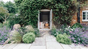 A garden entrance with a stone pathway leading to a door, surrounded by lush greenery and flowering plants. - Georgian Old Rectory with heated Pool
82  5 Star Reviews on Trip Advisor (Maidford, Towcester)