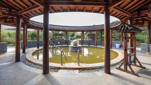 A circular pool with a stone centerpiece, surrounded by a wooden pergola structure. - Tangxi Hot Spring Resort (Chongren)