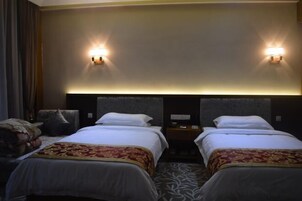 Habitación de hotel con dos camas, cabecero con iluminación integrada, mesita de noche y alfombra estampada.