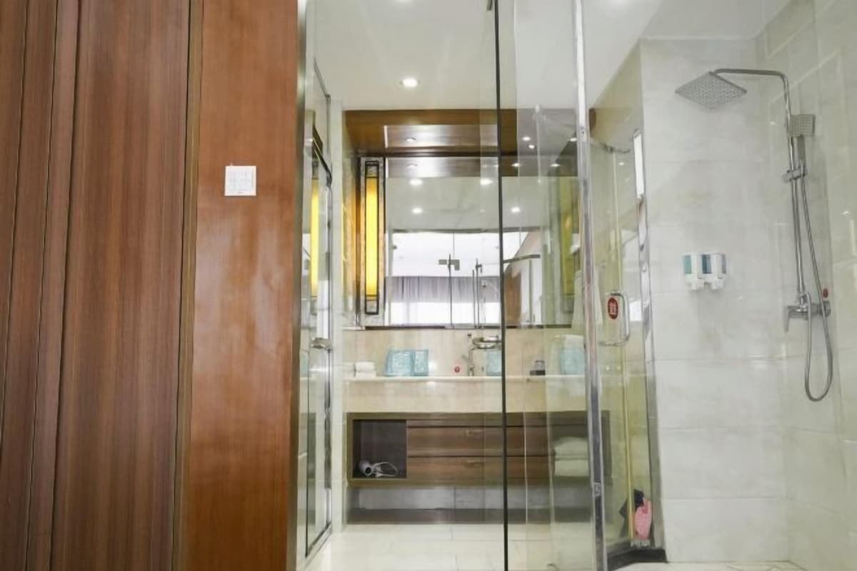 A modern bathroom with a glass shower enclosure, a wooden panel on one side, and a visible sink area.