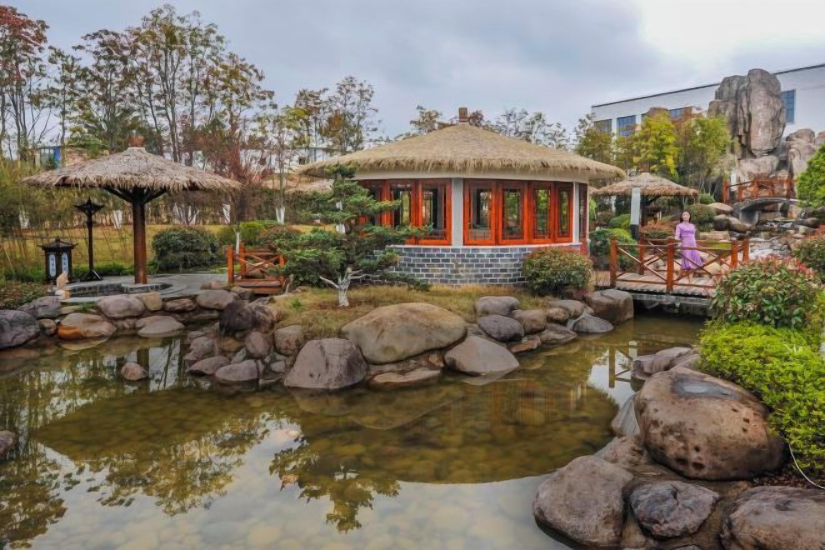A traditional-style building with a thatched roof, surrounded by a pond with rocks and greenery.