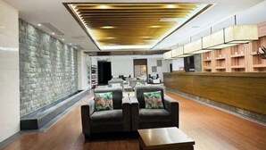 A modern lobby with a stone wall, leather sofas, a wooden reception desk, and a ceiling with recessed lighting. - Tangxi Hot Spring Resort (Chongren)