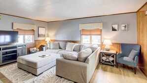 A modern living room with a sectional sofa, a flat-screen TV, and a small side table with a lamp. - Cozy Wisconsin Abode: Walk to Lake Michigan! (Algoma)