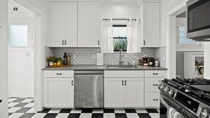 A modern kitchen with white cabinets, a stainless steel dishwasher, a black and white checkered floor, and a built-in stove. - The Birdhouse at The Birdbath Bungalows (Ventura)