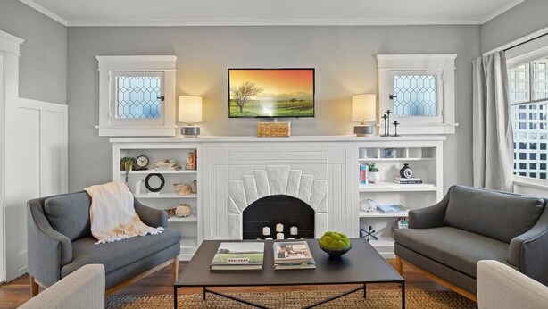 A living room with a fireplace, two sofas, a coffee table, and a television mounted above the fireplace. - The Birdhouse at The Birdbath Bungalows (Ventura)