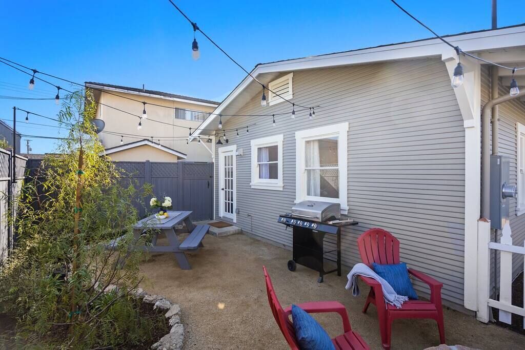 A backyard with a barbecue grill, picnic table, and red chairs.