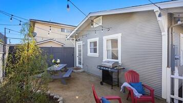 A backyard with a barbecue grill, picnic table, and red chairs.