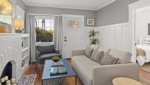 A living room with a sofa, armchair, coffee table, and a fireplace. - The Birdhouse at The Birdbath Bungalows (Ventura)