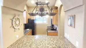 Eine Küche mit einer Granitinsel, zwei hohen Barstühlen, einer Schiffslenken-Dekoration und einem Chandelier.