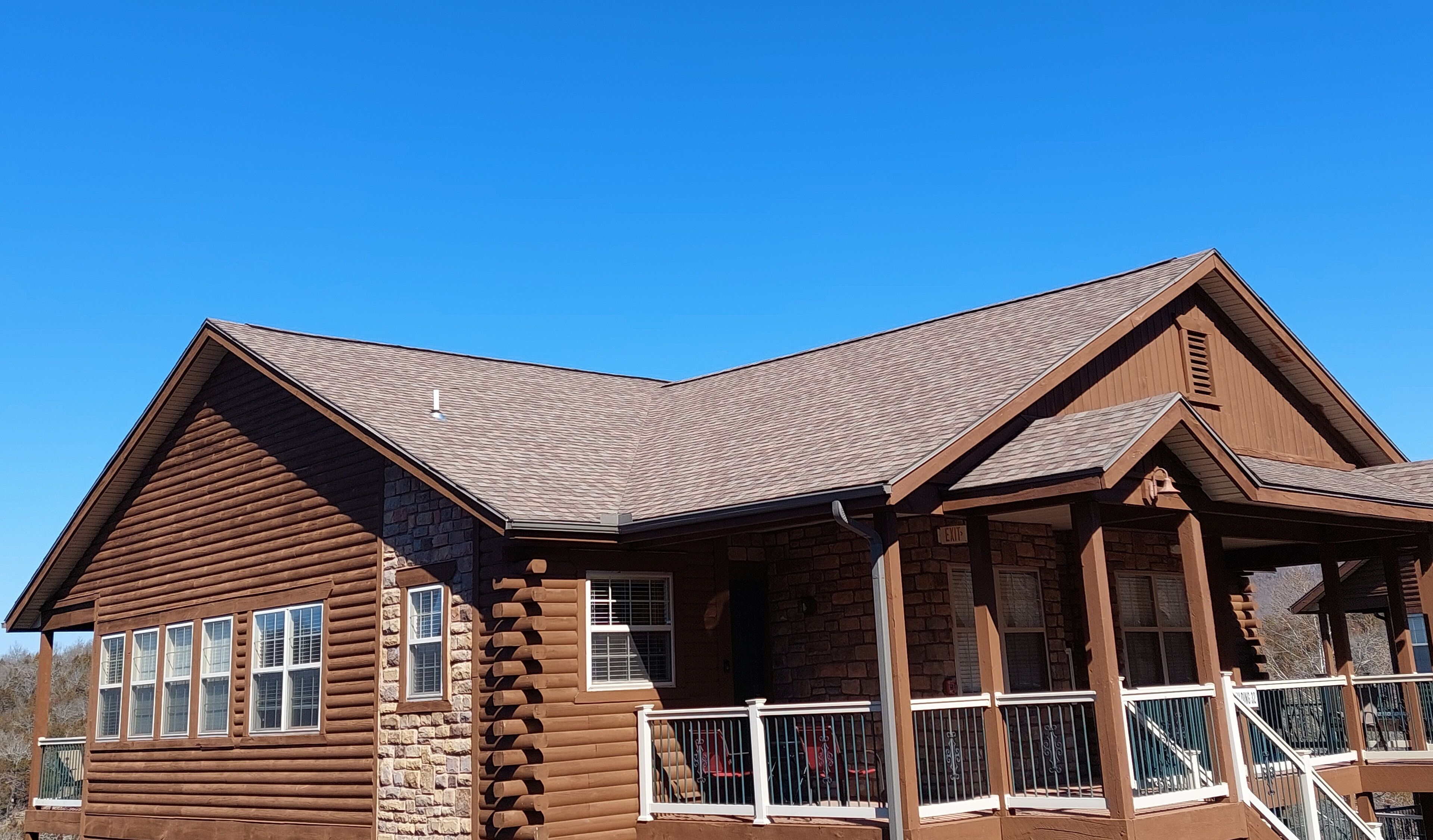 A log cabin with a stone foundation, a steeply pitched roof, and a porch with railings.