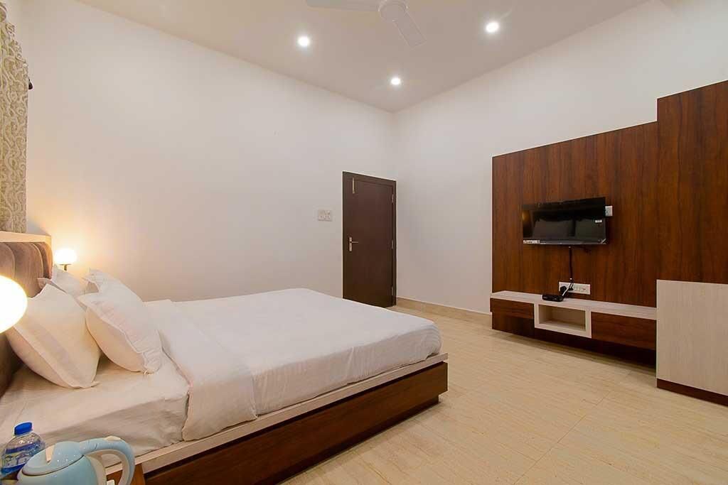 A modern bedroom with a bed, a TV mounted on a wooden panel, and a small bedside table.